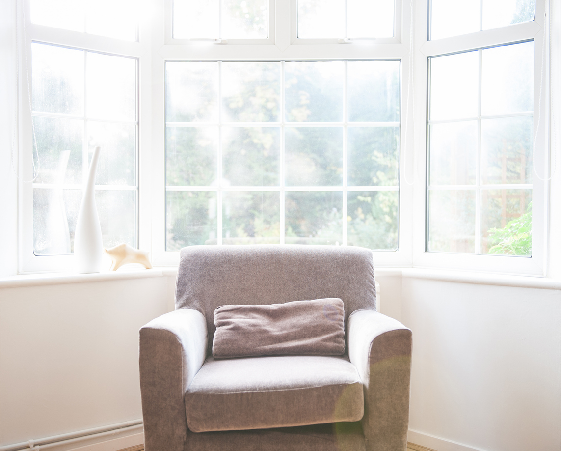 An armchair sits by a bright bay window, bathed in soft natural light. The space feels warm, calm, and inviting.